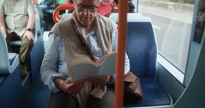 Senior man traveling while sitting  inside tram while reading a book 