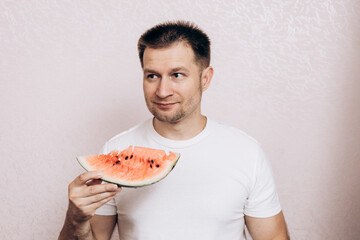A guy in a white T-shirt holds a ripe watermelon and eats it. Summer fruits from the garden