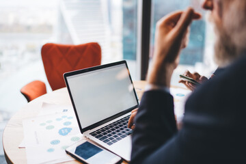 Crop colleagues using laptop and documents while sitting at table