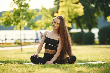 On the yoga mat. Beautiful young woman in sportive clothes is in the park at sunny daytime