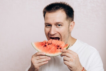 A guy in a white T-shirt holds a ripe watermelon and eats it. Summer fruits from the garden