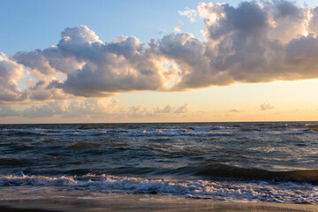 Beautiful sunset over the sea. Waves, clouds and black sand