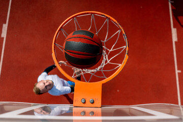 Close-up of a basketball ring into which a tall guy basketball player throws the ball from below...