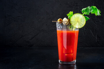 Bloody Mary cocktail with ice on a black background. Spicy tomato juice with alcohol, lime, celery, and pickles, with a place for text