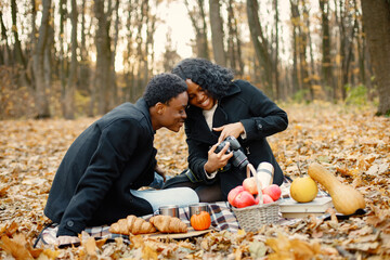 Loving black couple have a picnic in autumn park and take a photo