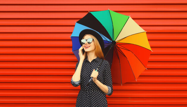 Happy smiling young woman calling on phone with colorful umbrella on red background