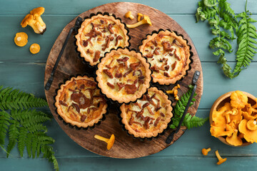 Savory hands pie with chanterelle mushrooms, cream and cheese on cutting board on rustic old wooden table background. Homemade tarts with seasonal chanterelle mushrooms. Rustic style. Top view.