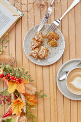 Atmospheric time for yourself - coffee time outside with a book - cutting doughnut and cappuccino among fall decorations. Atmospheric coffee time, guilty pleasure.
