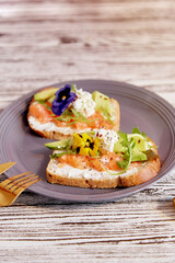 Healthy breakfast - toasts with salmon, avocado and edible flowers. Pescetarian diet.