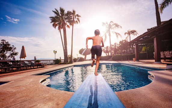 Boy run on diving board jumping to pool at sunset