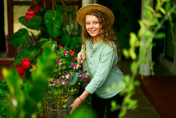 Young woman stands in garden planting flowers in pots smiles and looks at camera. Junior female gardener with gardening tool in her orchard taking care of potted plants. Farming and gardening concept