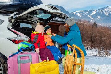 Mother help dress kids sitting in car trunk over snow mountain
