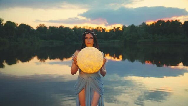 Fantasy woman caught glowing moon holding planet in hands. Mystery Girl fairy tale elf beauty face makeup, river nymph wet blue dress, stands in water dark lake summer nature. Lady queen night. art 4k