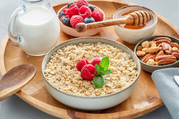 Bowl of porridge or oatmeal with different ingredients on wooden tray. Breakfast serving.