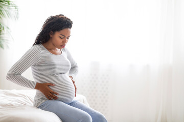 Braxton Hicks contractions. Young black pregnant woman suffering abdominal ache at home