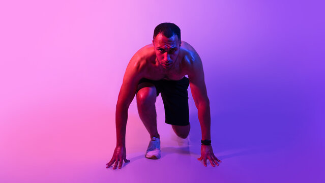 Black athlete man standing in crouch start position, neon light