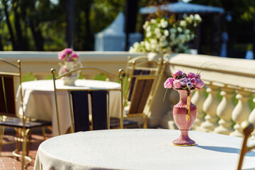 The tables are decorated with vases of fresh flowers on the outdoor terrace of the restaurant