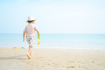 Asian boy with sunglasses and a hat playing on the beach.