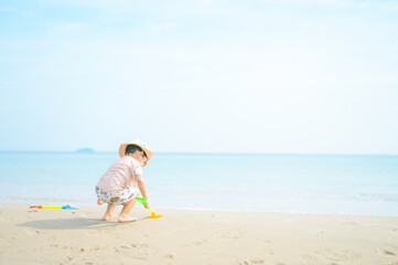 Obraz premium Asian boy with sunglasses and a hat playing on the beach.