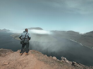 Young adult stands atop a rocky cliff, marveling at the breathtaking view of the Faroe Islands