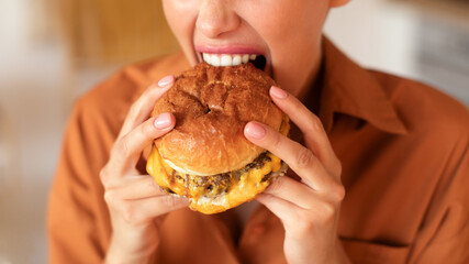 Closeup shot of hungry unrecognizable lady biting, eating tasty burger, enjoying fast food cheat...