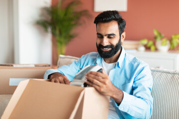 Obraz premium Indian buyer man unpacking box with new device at home
