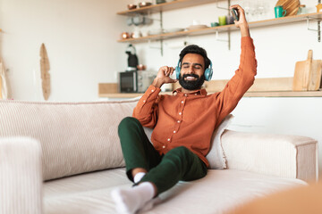 Relaxed Indian guy with headphones and phone enjoying music indoor