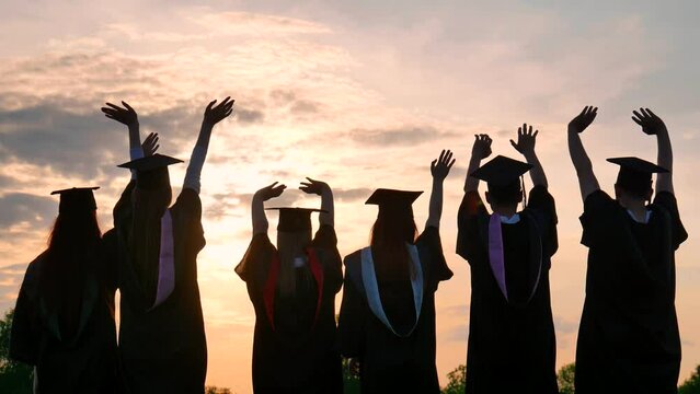 Silhouettes of graduates in black robes wave their arms against the evening sunset and toss their caps. - Powered by Adobe