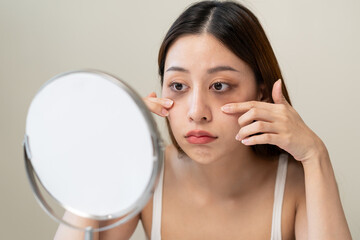lack of sleep problem, Worried Asian young woman pointing finger at dark circles under her eyes