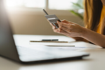 Close up view hands of young woman holding a credit card and doing bank transactions via mobile phone application at home