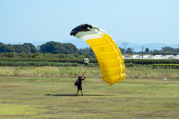 Stunning view of a skydiver with a yellow parachute landing on a green lawn during a sunny day.