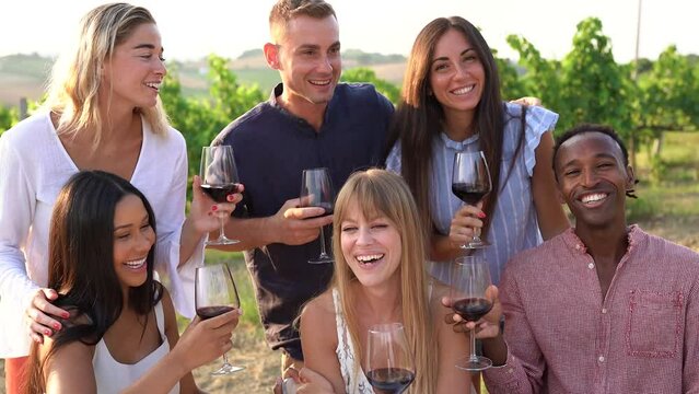 Happy group of adult friends cheering with red vine inside wineyards - Multiracial people enjoy summer vacation in nature
