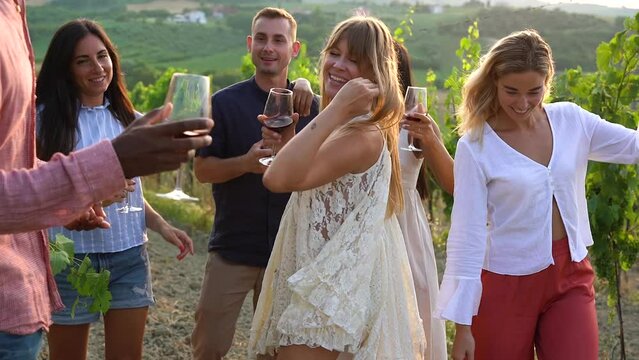 Multiracial people dacing together at wineyard holding glasses of red vine - Diverse friends enjoy day together outdoor during summer time
