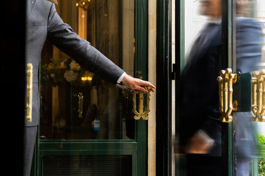 Luxury service gesture &ndash; Business man holding a door handle with blurred motion of a guest entering a high-end establishment