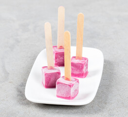 Vegan dessert. Mini Black currant ice cream in the shape of a cube on a wooden stick. On a plate. Light gray background