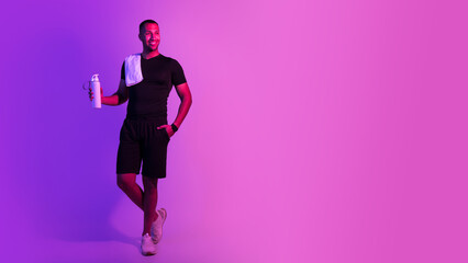 African American athletic guy holding fitness bottle on purple background
