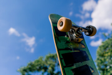 Close-up of a skateboard that a skateboarder is holding in his hand in the air against the background sky 
