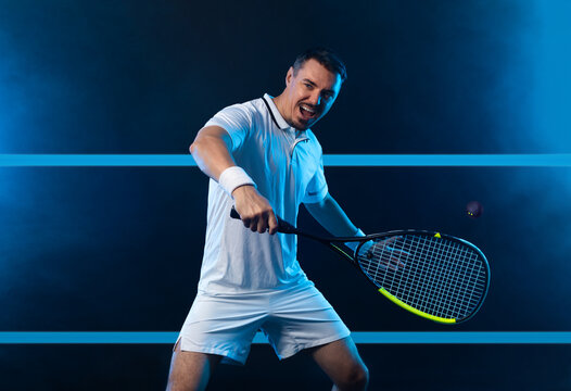 Squash player on a squash court with racket. Man athlete with racket on court with neon colors. Sport concept. Download a high quality photo for the design of a sports app or betting site.
