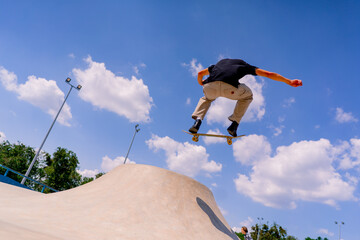 A young guy skater does a stunt on the edge of a skatepool against a backdrop of sky and clouds at a city skate park 