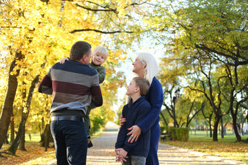 A family of four poses in an autumn park. The father holds the youngest son in his arms, the mother and elder brother look and smile
