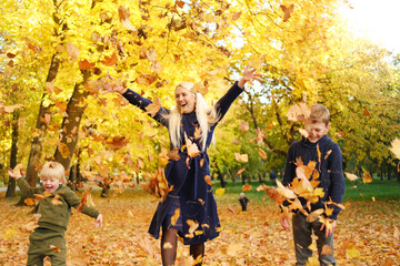 Mother with children throw autumn leaves up and have fun