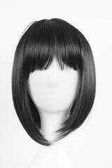 Natural looking black wig on white mannequin head. Medium length straight hair with bangs on the metal wig holder isolated on white background, front view