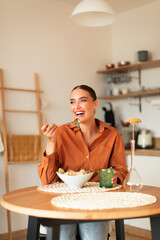 Happy young lady enjoying her home cooked caesar salad, sitting at table in kitchen interior, vertical shot, copy space - obrazy, fototapety, plakaty