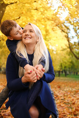 Fototapeta premium Mother and son in autumn park. Son kisses mother, mother smiles
