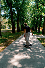 Fototapeta premium young guy skater rides a skateboard on the path of the city park against the background of trees and sky
