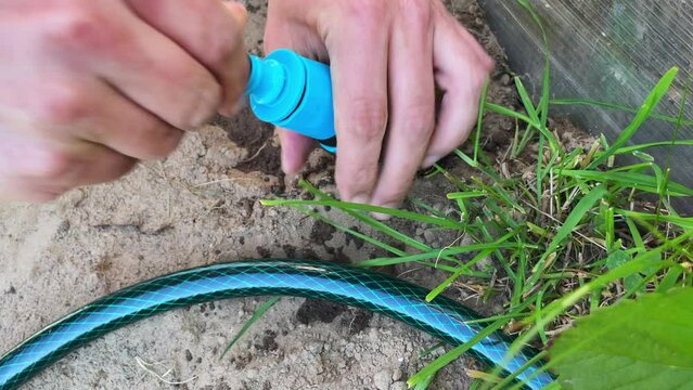 Close-up of a plumber installing a hose clamp while connecting a submersible pump in a garden area. Outdoor plumbing repair. The water hose is clamped with a hose clamp.