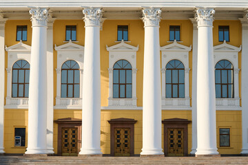 Obraz premium Front part of munucipal or cultural institution with white plaster columns, row of long arch shaped windows, wooden doors and yellow walls