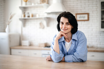 Fototapeta premium Portrait of smiling woman standing in kitchen, looking at camera