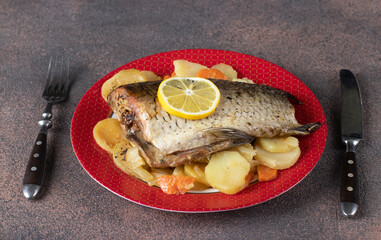 Carp baked with potatoes, served on a plate on a brown background