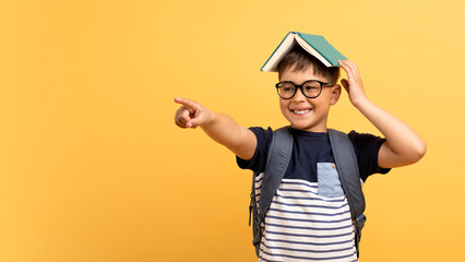 Excited school aged kid boy with book on his head